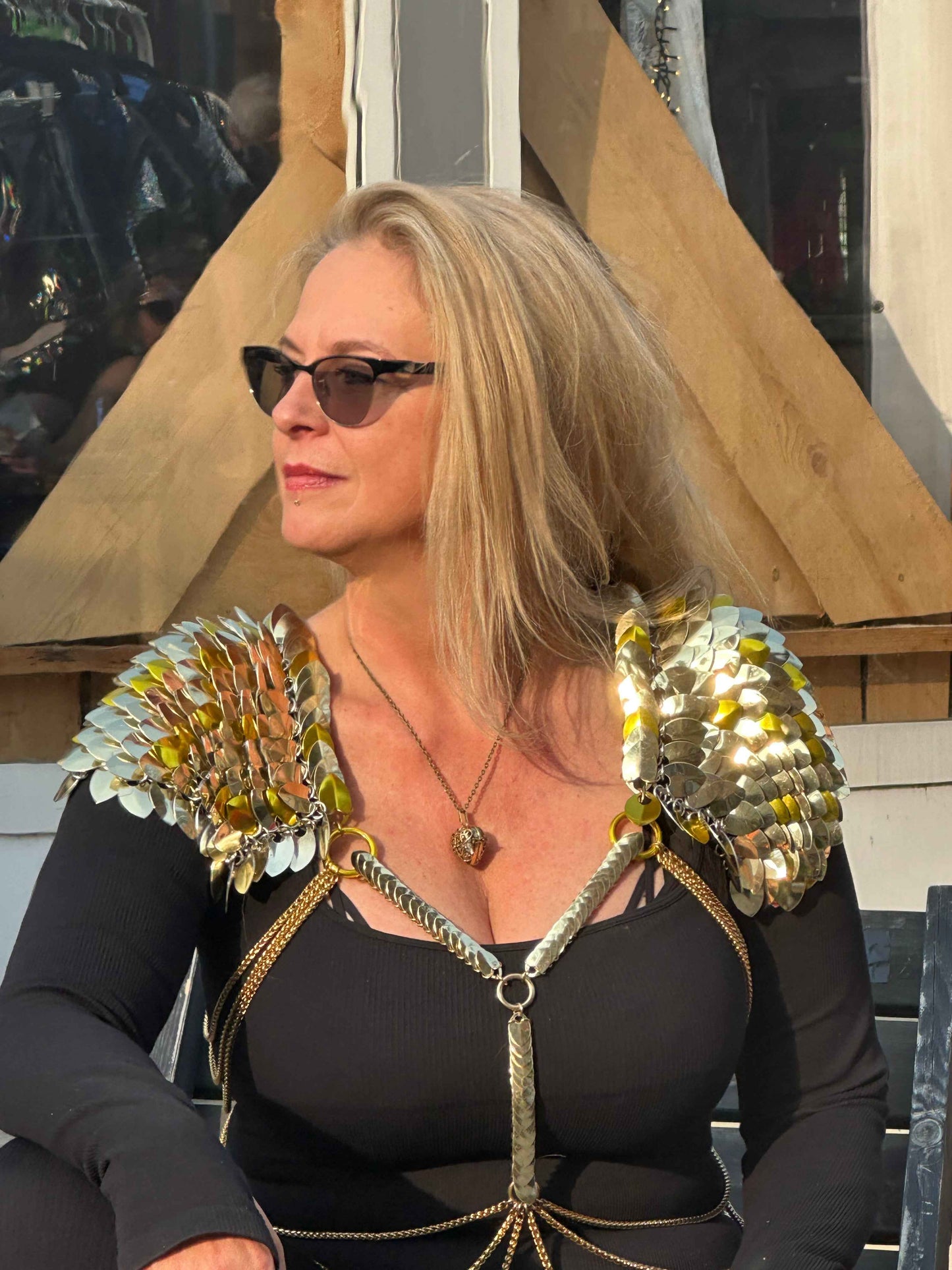 Blonde woman wearing metallic gold scale armor shoulder pauldrons and black top, confident mood