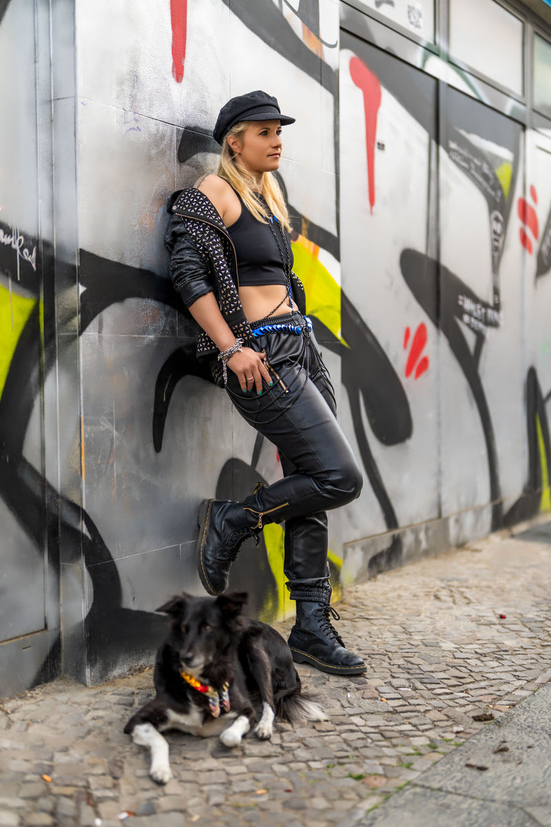 Young woman in black leather pants, crop top, and jacket with black dog, urban street style, confident