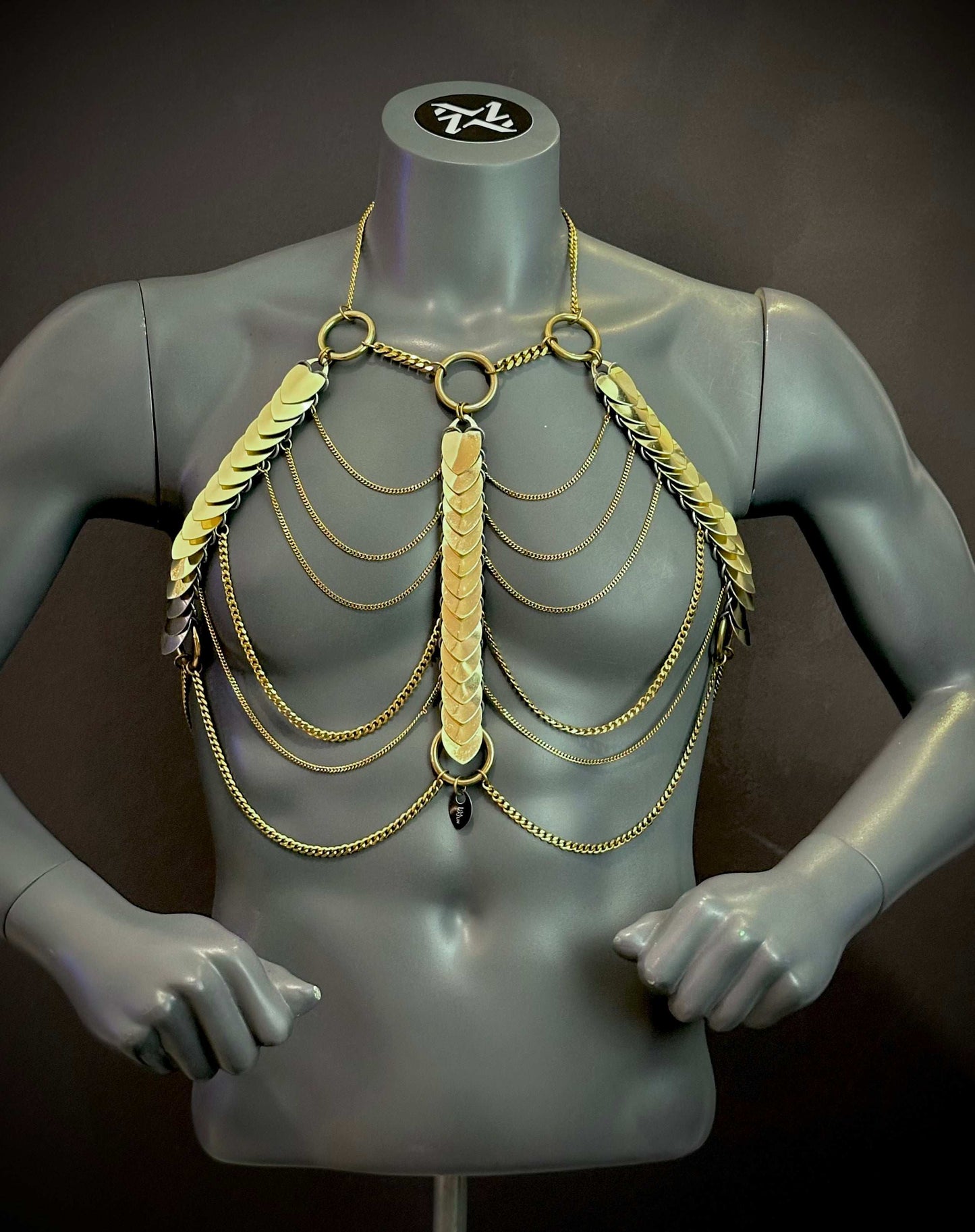 Goldener Aphrodite Fire Harness mit Ketten und Plättchen auf grauem Männer-Mannequin, elegant und kraftvoll