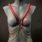 Ariv Harness Gold und Rot mit Ketten auf grauem Schaufenster, elegant und kraftvoll