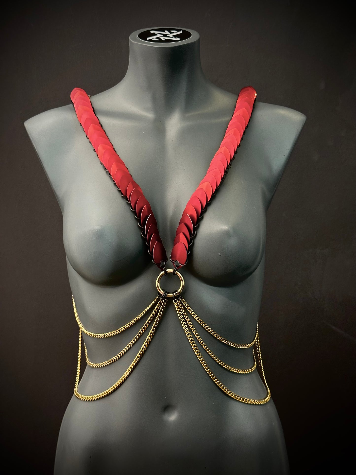 Ariv Harness Gold und Rot mit Ketten auf grauem Schaufenster, elegant und kraftvoll