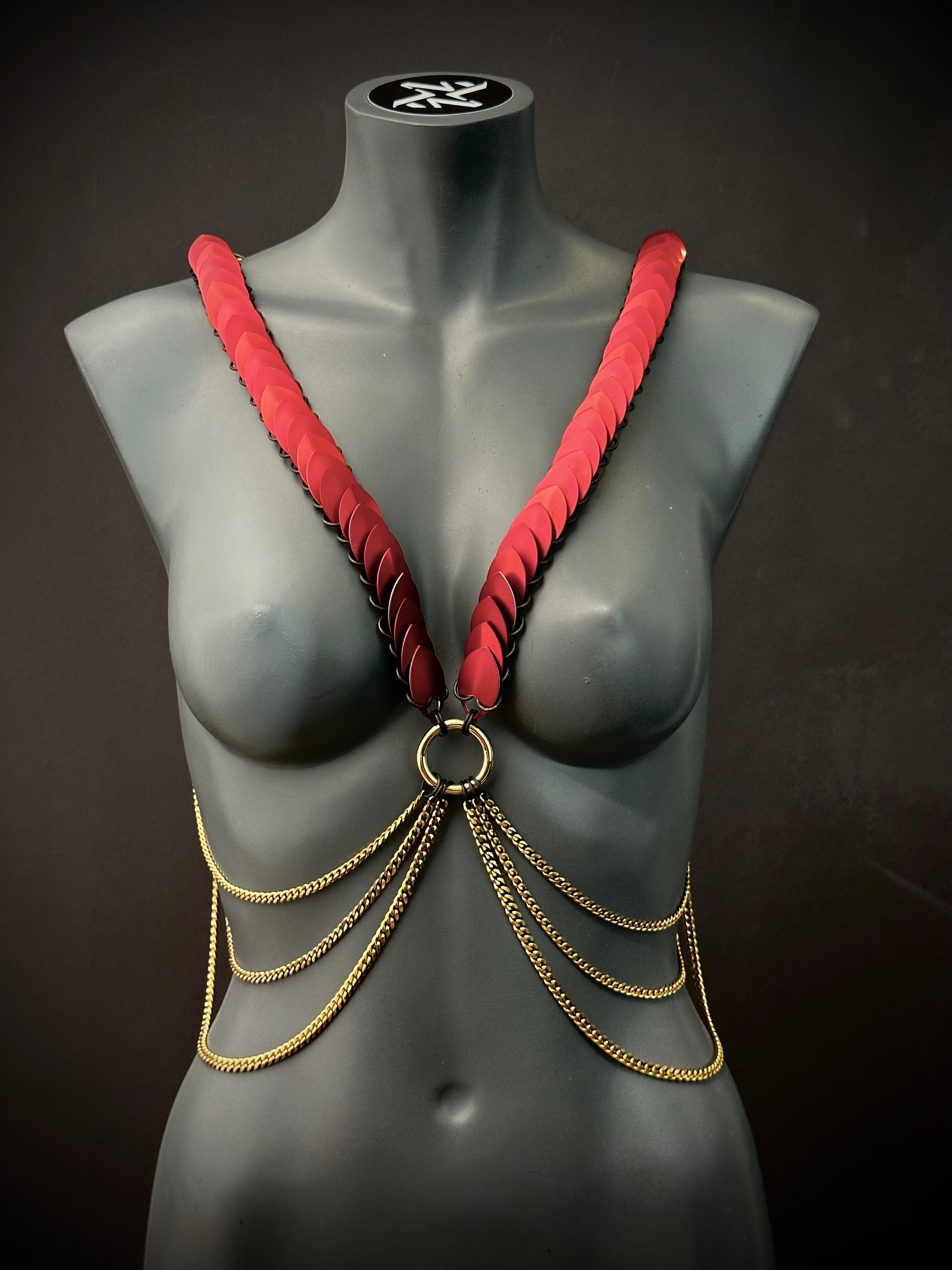 Ariv Harness Gold und Rot mit Ketten auf grauem Schaufenster, elegant und kraftvoll
