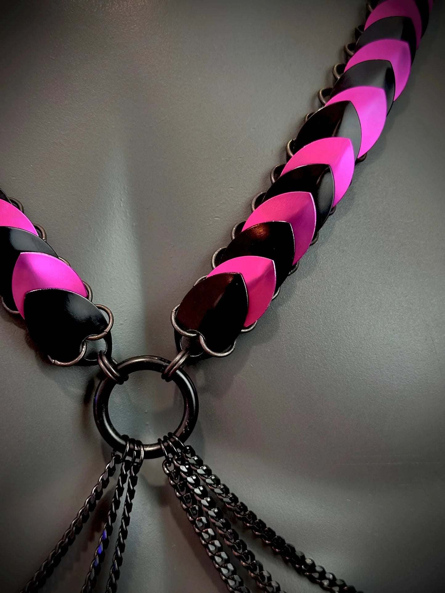 Ariv Harness schwarz pink mit Ketten und glänzenden Metallplatten, kraftvoll und stylisch