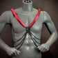 Harness mit schwarzen Ketten und roten Plättchen, stylisch und provokativ am grauen Torso