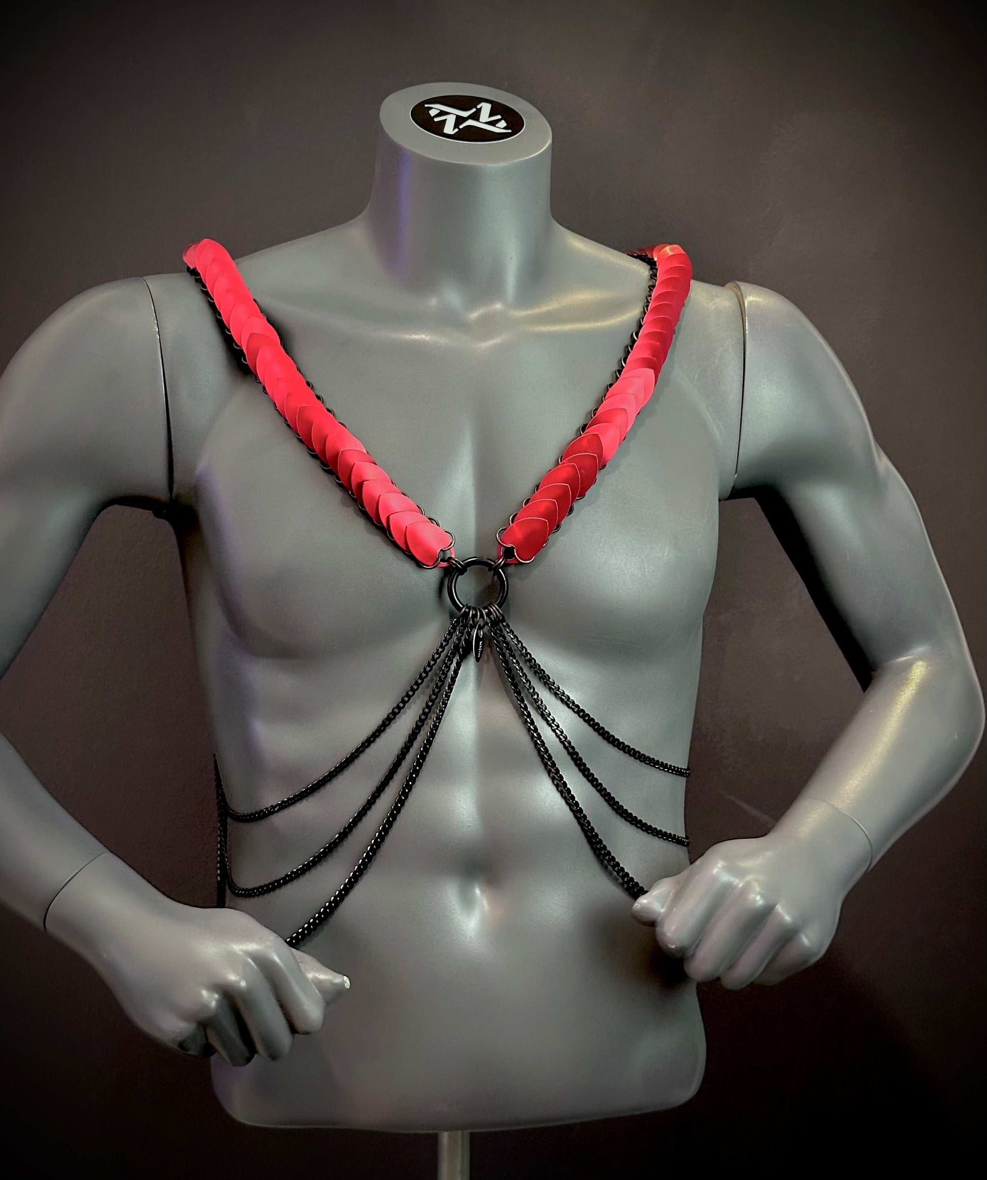 Harness mit schwarzen Ketten und roten Plättchen, stylisch und provokativ am grauen Torso