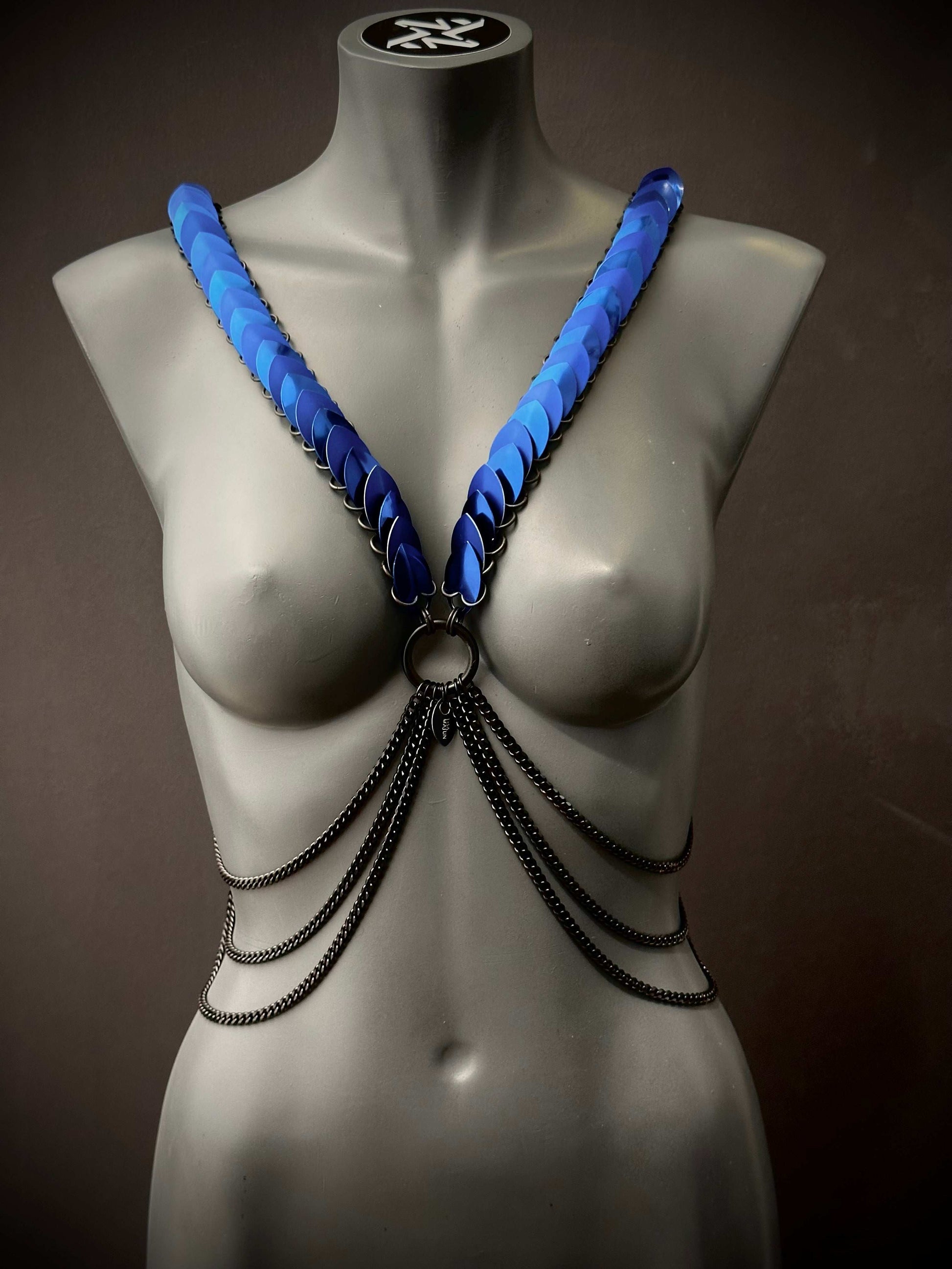Ariv Harness blau mit Metallketten, modisch und kraftvoll, ausdrucksstark am grauen Schaufenster