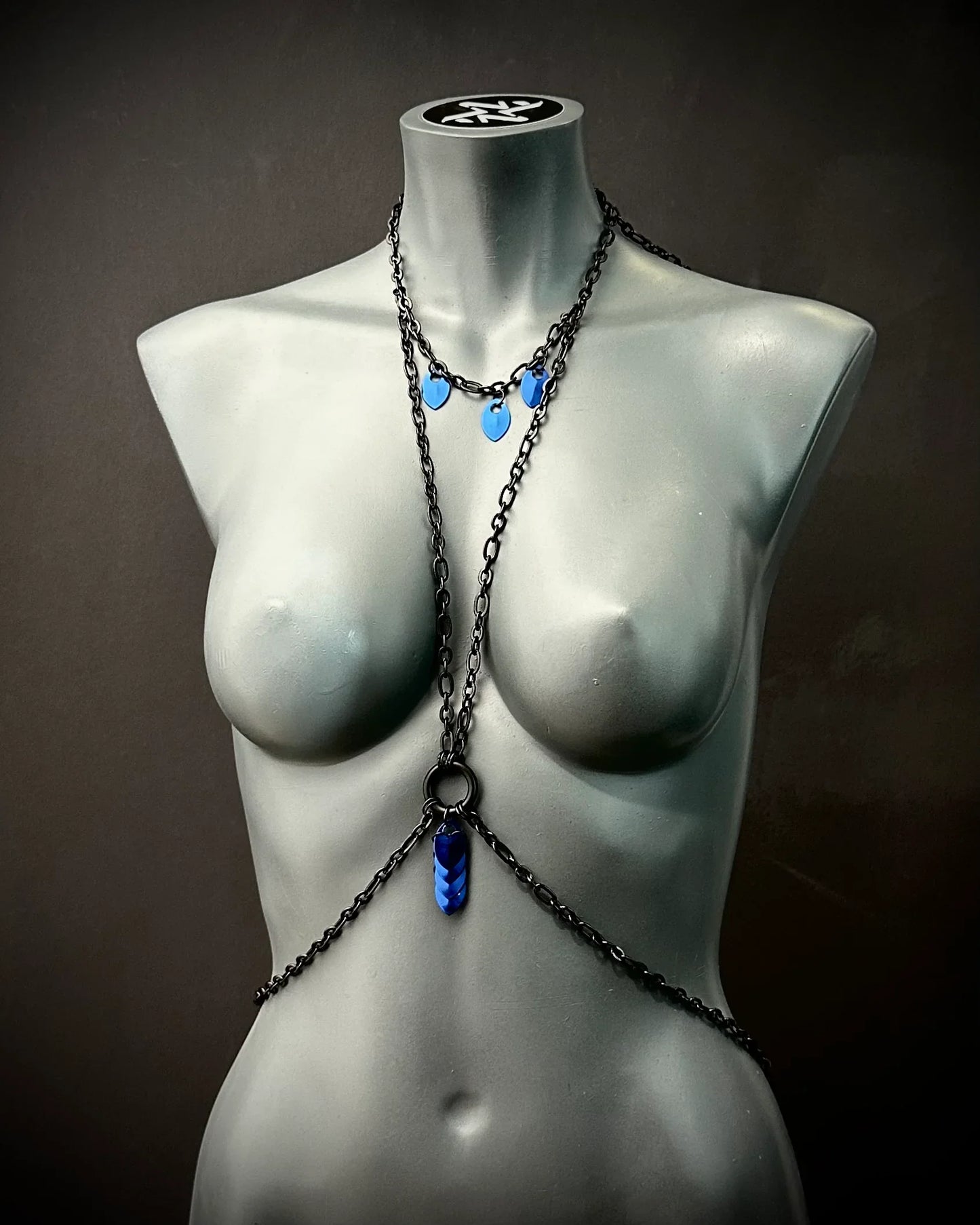 schwarze Bodychain mit blauen Anhängern am grauen Frauenfigur-Mannequin, moderner Stil, elegant