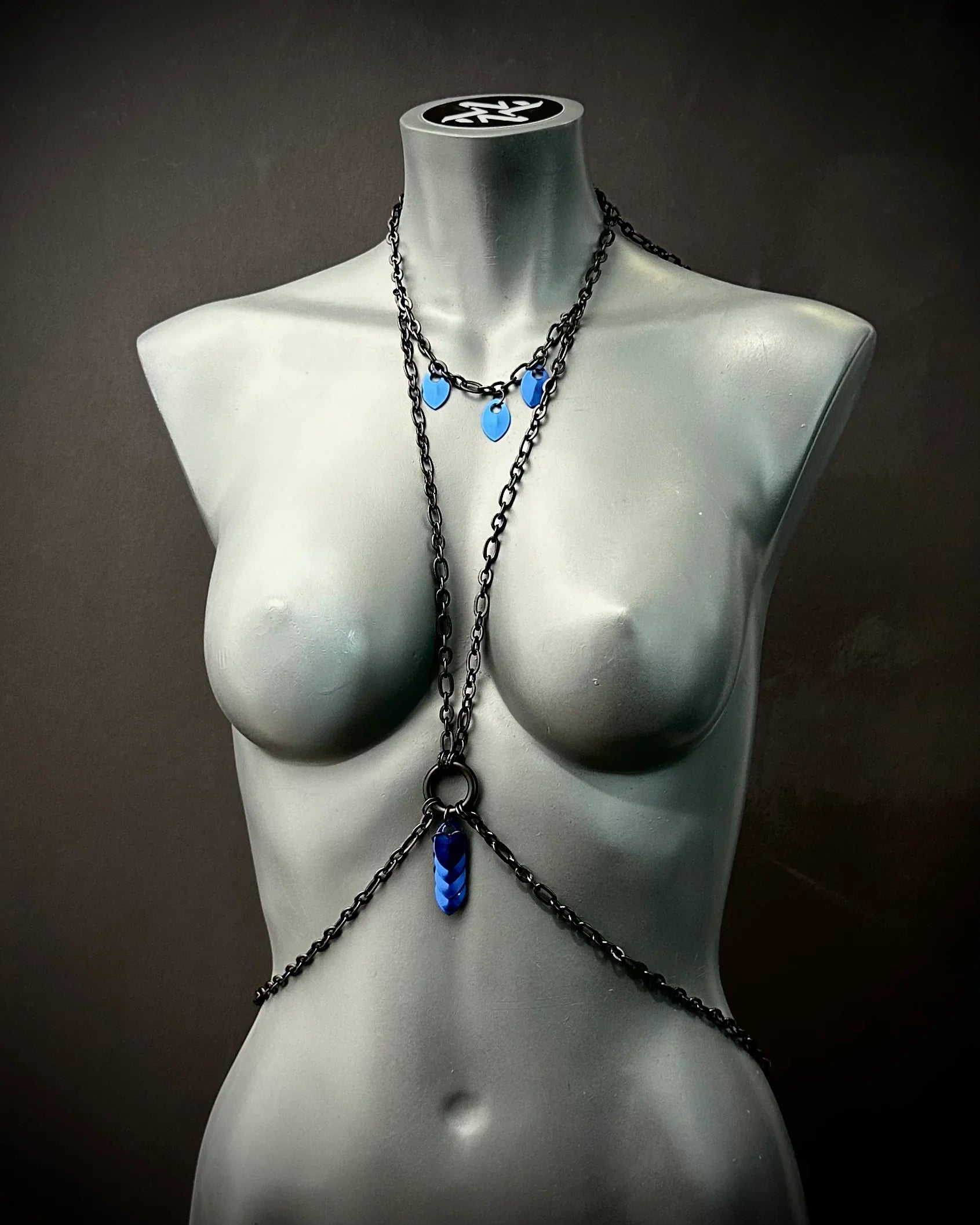 schwarze Bodychain mit blauen Anhängern am grauen Frauenfigur-Mannequin, moderner Stil, elegant