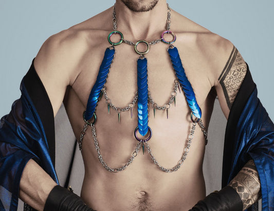 Moderne blaue Body Chains aus Metall am Oberkörper eines tätowierten Mannes mit schwarzer Jacke zeigen Stil und Selbstbewusstsein