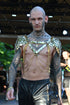 Tattooierter Mann im goldenen Ketten- und Schuppen-Top, schwarzer Lederhose, kraftvoller Stil und intensiver Ausdruck